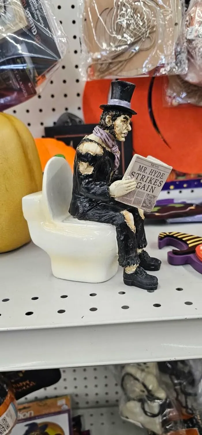 Weird thrift find of a monster figurine sitting on a toilet reading a newspaper