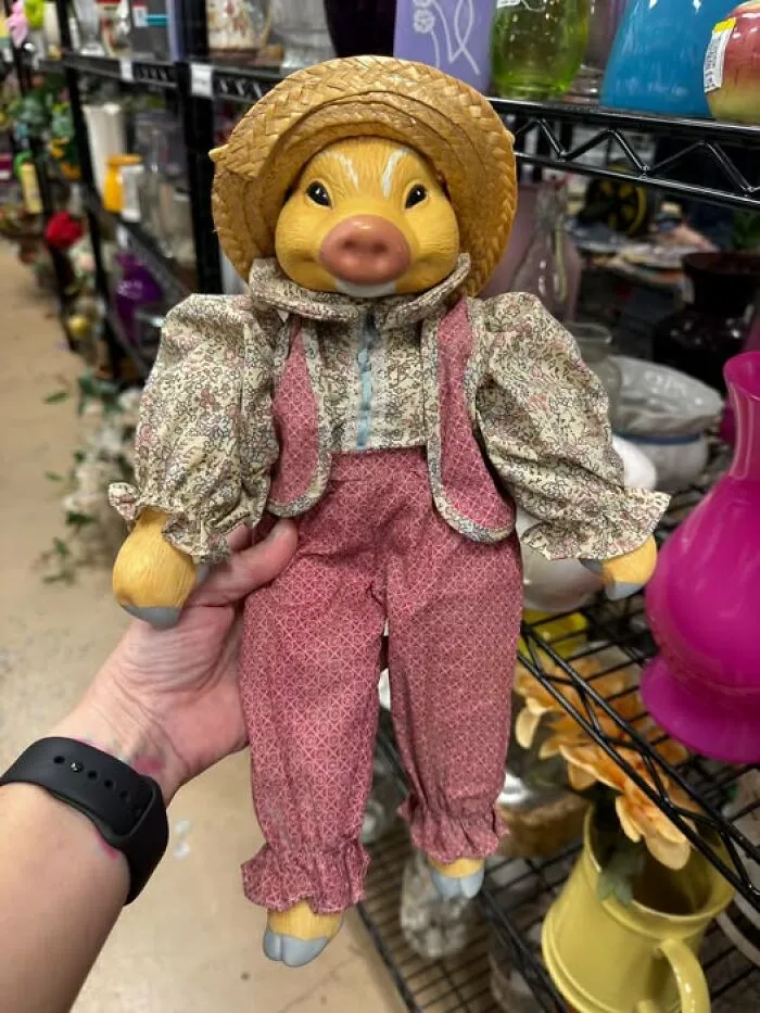 A hand holding a pig doll dressed in countryside attire, a unique thrift find