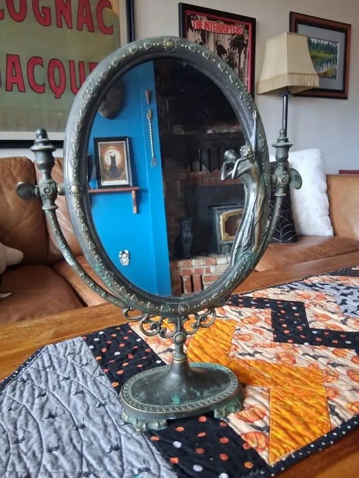Ornate bronze vanity mirror with a sculpted figure, an ornate vintage thrift find on a table runner