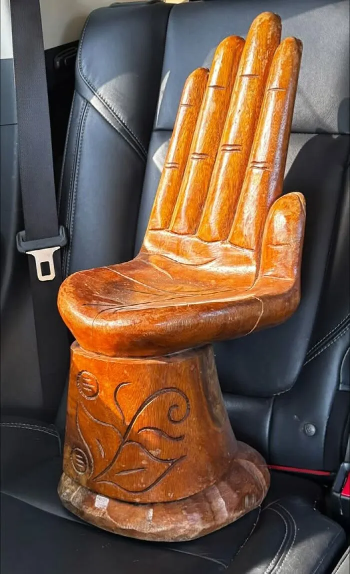 Hand-carved wooden hand chair sitting on a car seat, a unique item among thrift finds.