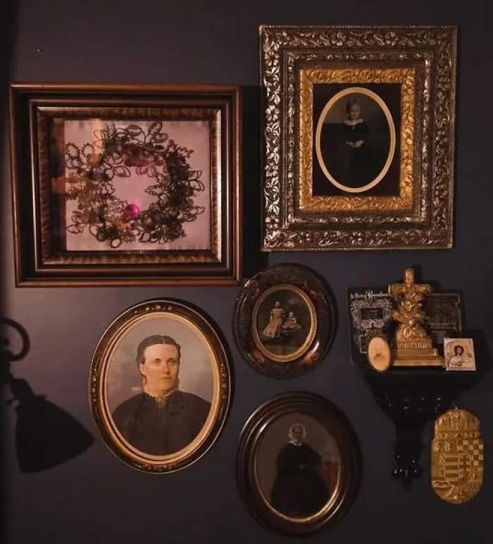 Collection of vintage framed portraits and artwork displayed on a dark wall as unique thrift finds.