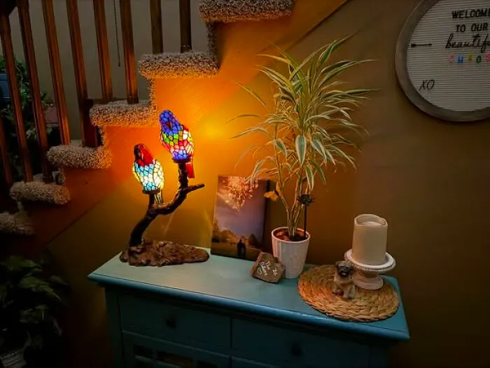 Stained glass parrot lamp found as a unique thrift find, displayed on a wooden table next to a plant.