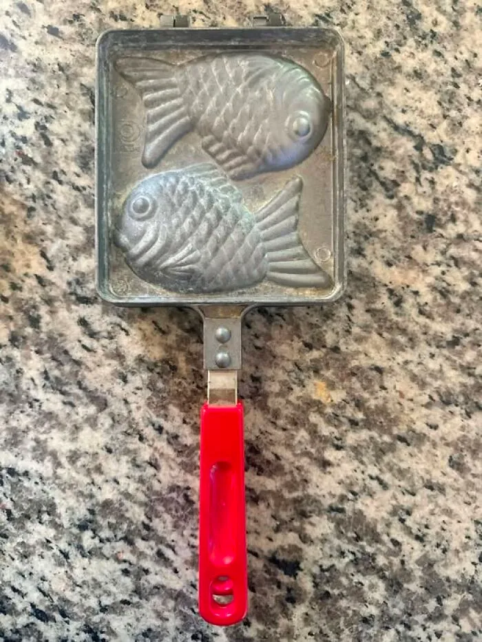 A vintage fish-shaped waffle iron maker resting on a granite countertop, a cool thrift find.