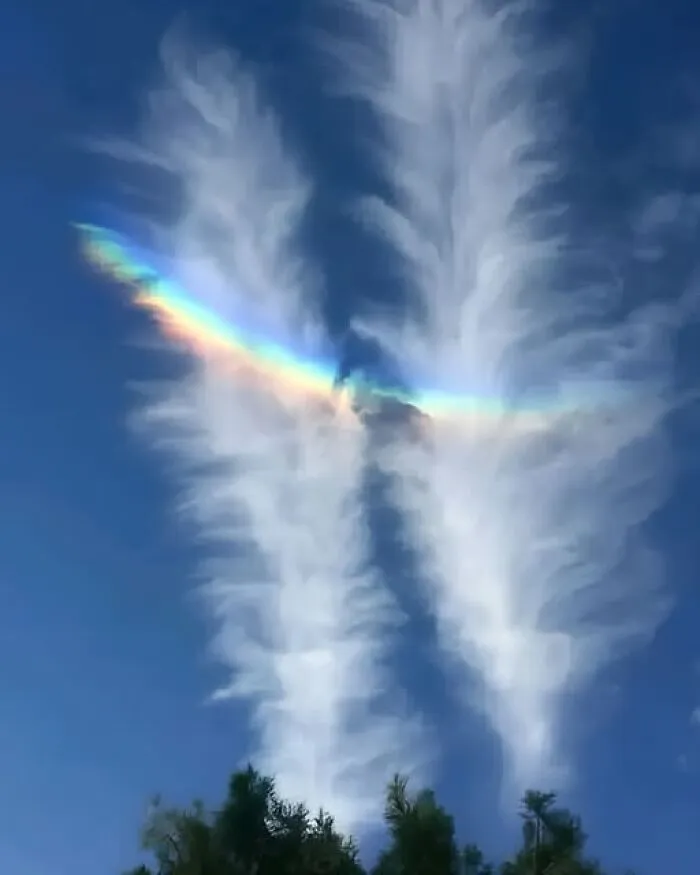 Rainbow light shining through two tall clouds, capturing interesting photos of sky phenomena.