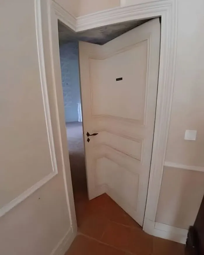 Odd photos of an unusual interior white door bent at a ninety degree angle to fit a corner.