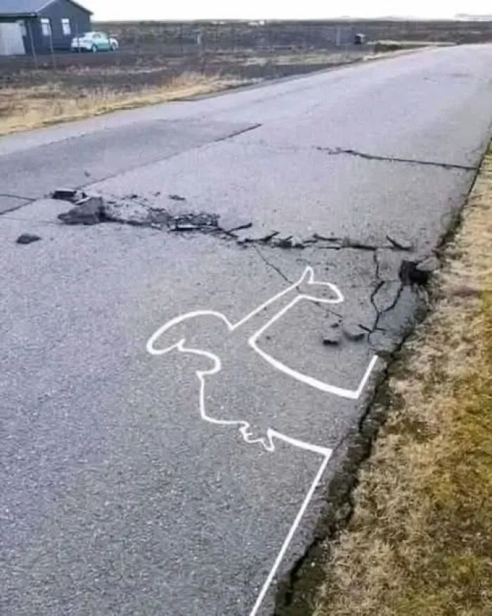 An interesting photo of a white line on a road painted around a crack, making an odd shape.