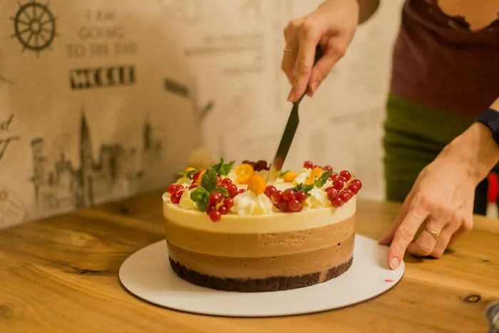 Person cutting a fancy layered cake decorated with berries, celebrating a weird at work event.