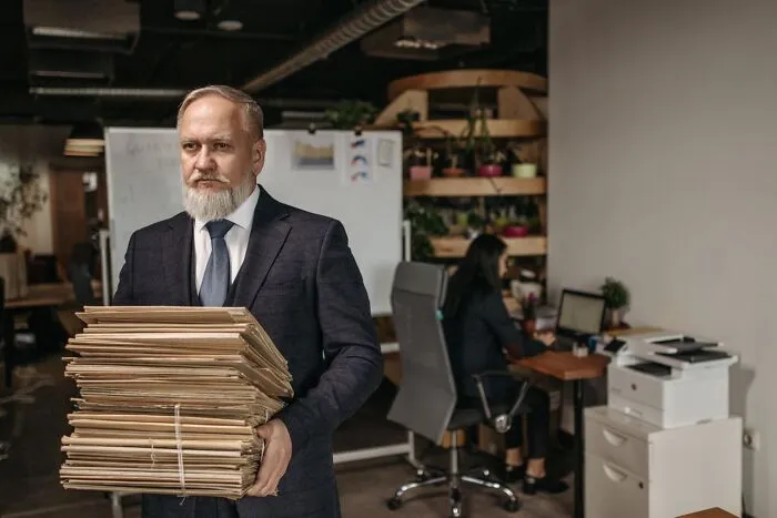 Man in a suit carrying a massive stack of folders, showcasing weird at work workload habits