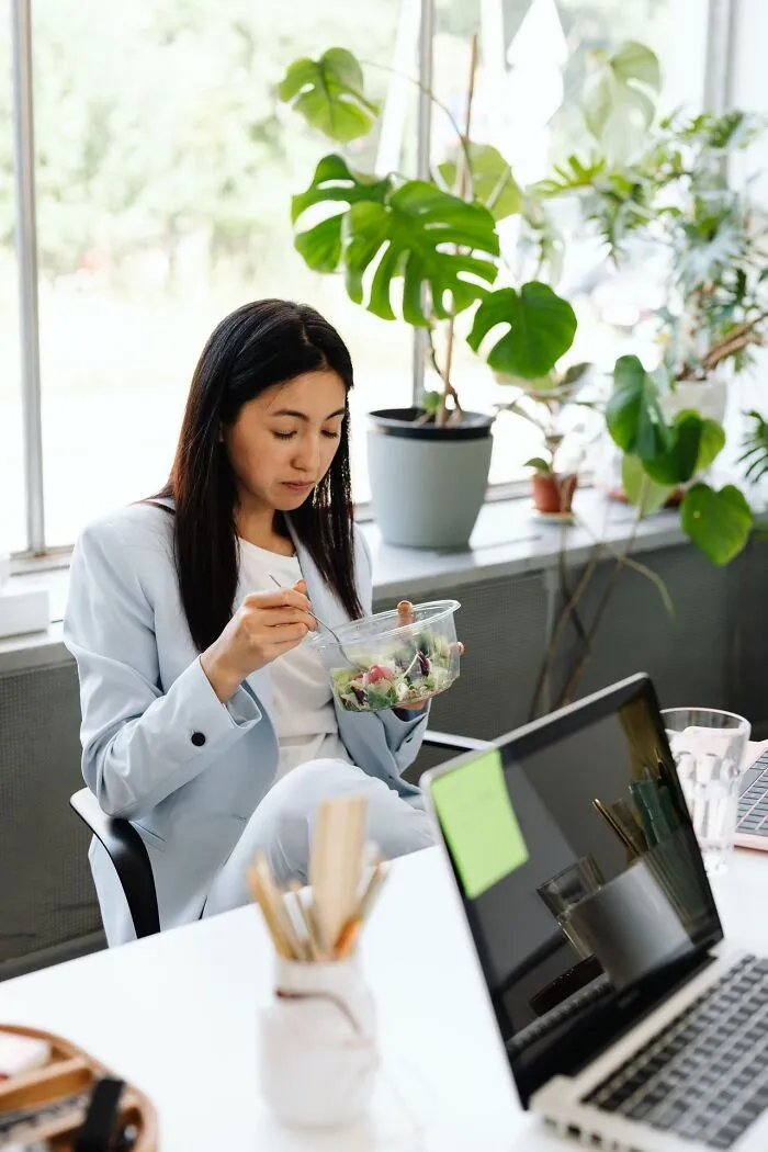 Woman sitting at her office desk eating a salad, representing weird at work lunch breaks