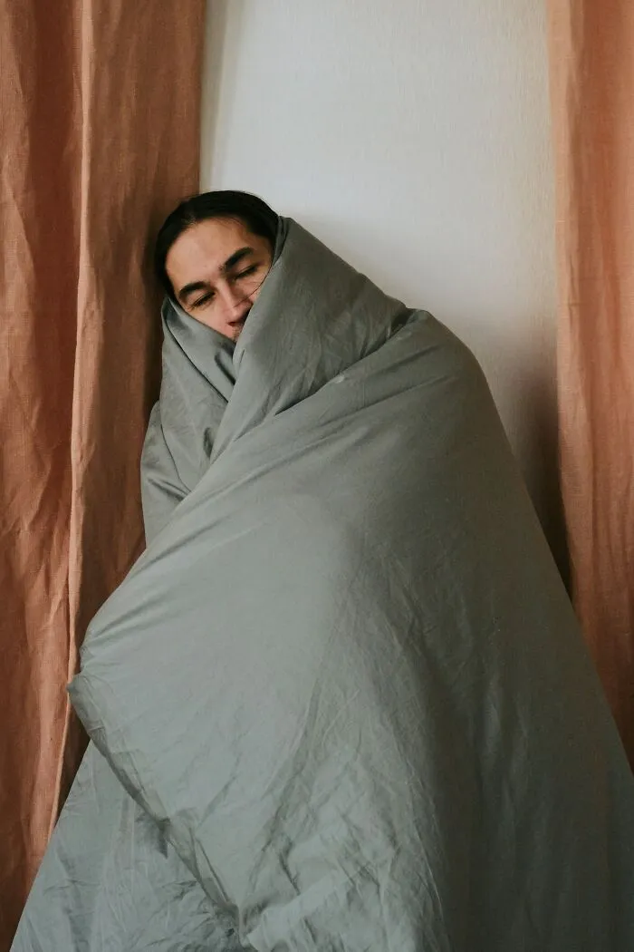 A person wrapped completely in a grey blanket sitting quietly, looking weird at work.