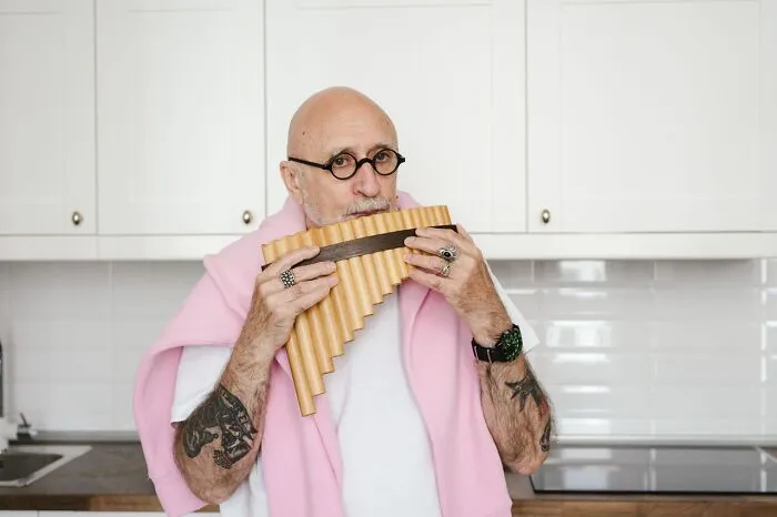 An older man playing a pan flute in the kitchen, acting weird at work during his break.