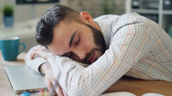 A tired man sleeping on his laptop keyboard during work hours