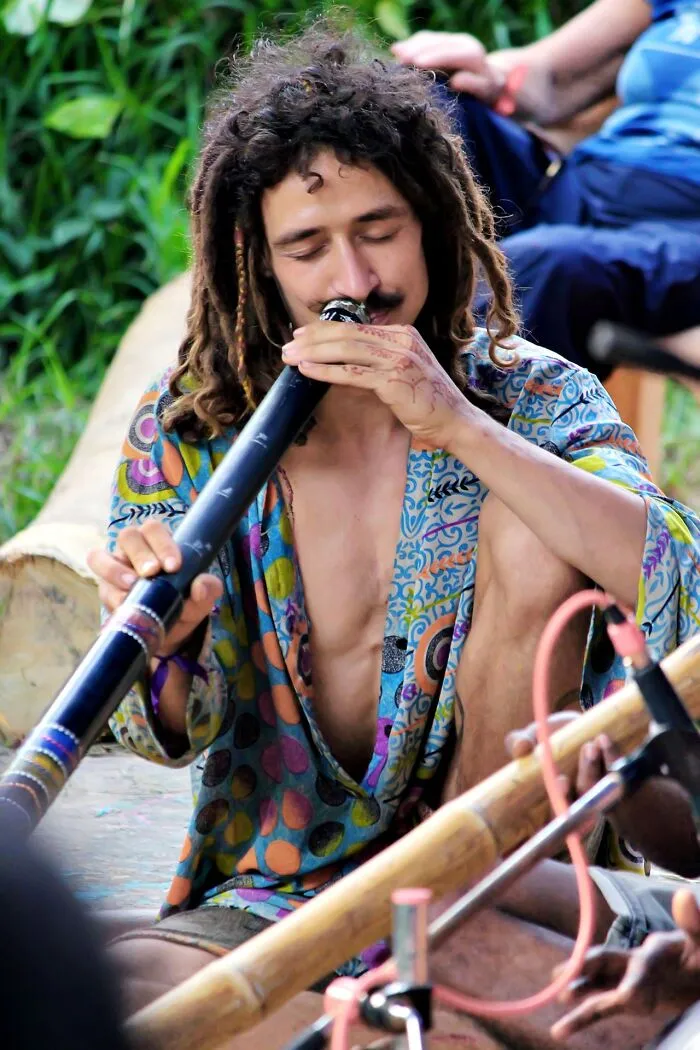 A man with dreadlocks playing a didgeridoo outdoors, showcasing weird at work moments.