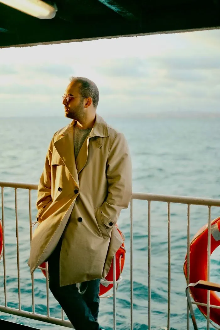 A man wearing a trench coat standing on a boat deck representing weird at work behaviors.