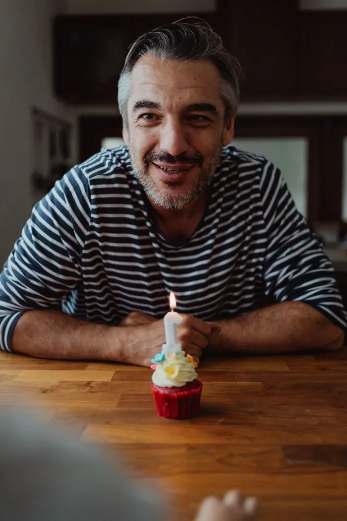 A smiling man behind a cupcake with a lit candle, showing weird at work behavior.