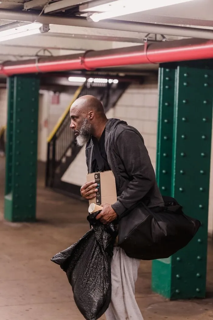 A man carrying bags and a package in a subway station, showcasing weird at work moments.