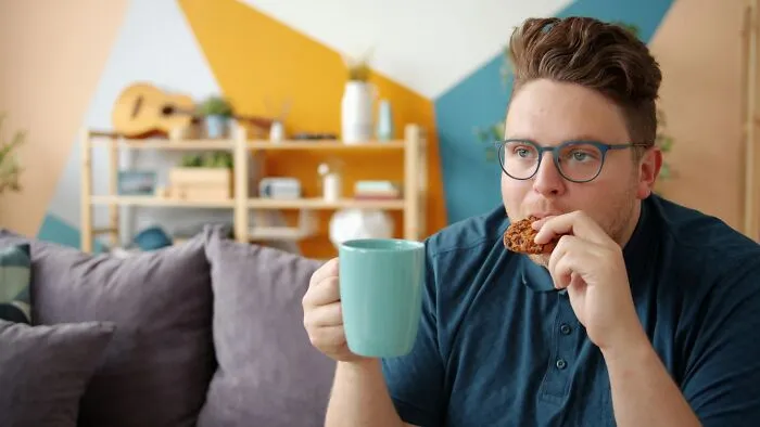 A man eating a cookie and drinking coffee in a colorful living room, showing weird at work habits.