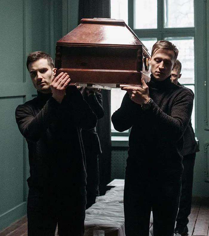 Pallbearers carrying coffin in a dimly lit room funeral job