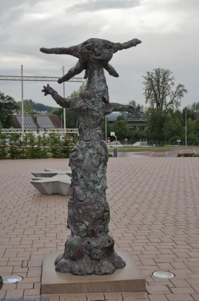 An abstract, rough-textured bronze sculpture in a paved plaza, showcasing a bizarre public art style.