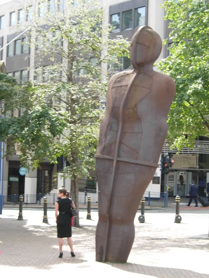 An abstract tall metal figure standing on a city street, showcasing modern public art