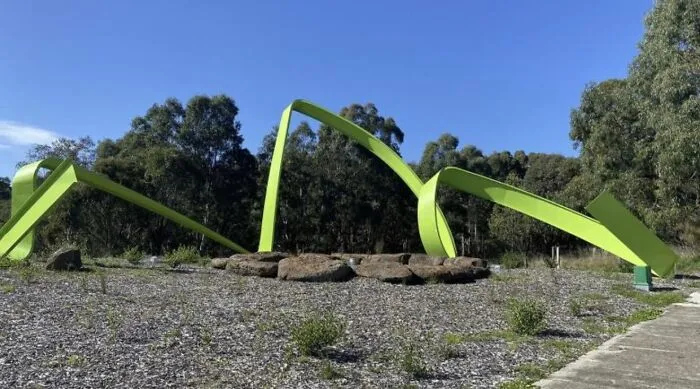 A large abstract green ribbon structure representing modern public art in an outdoor park