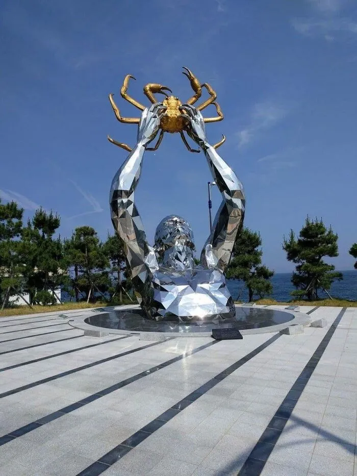 A metallic sculpture of a figure emerging from the ground holding a golden crab, as a piece of public art.