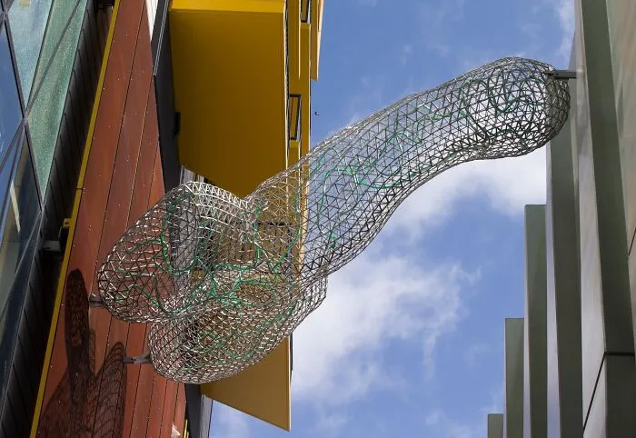 A wireframe phallic sculpture attached to a building, showing bizarre public art.