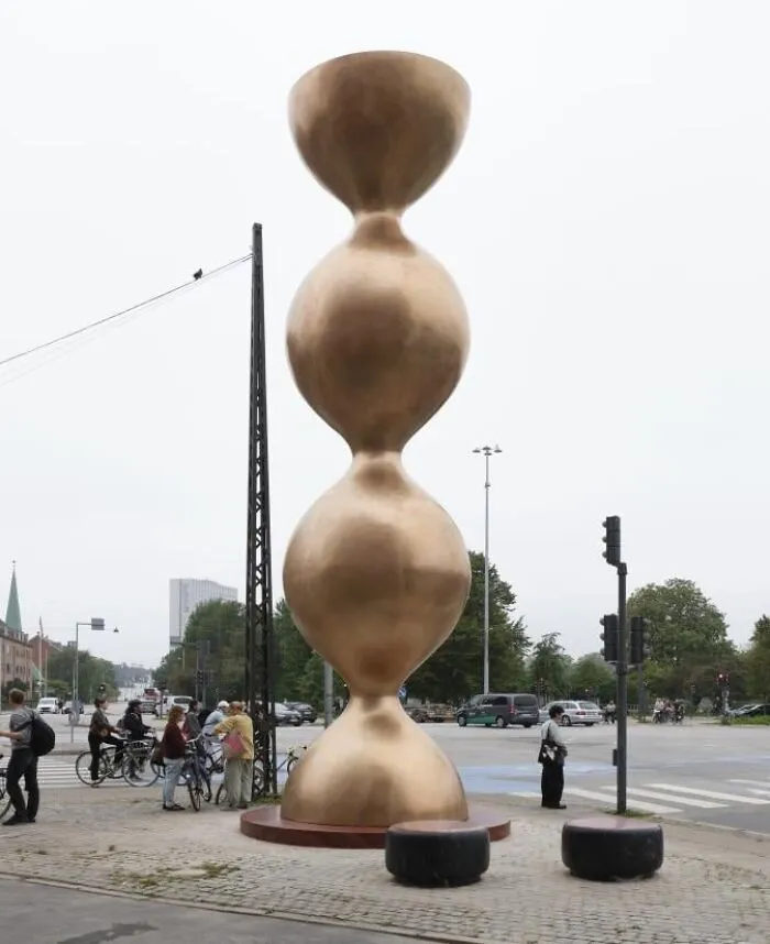A tall, bulbous golden tower sculpture on a city street, demonstrating examples of public art.
