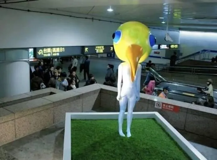 An unusual yellow bird-headed human figure standing in a subway station, showcasing bizarre public art.