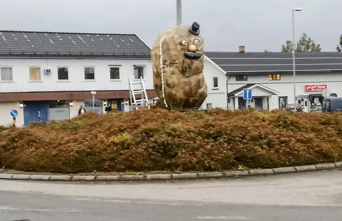 A large potato statue with a face and hat, showcasing bizarre public art in a roundabout
