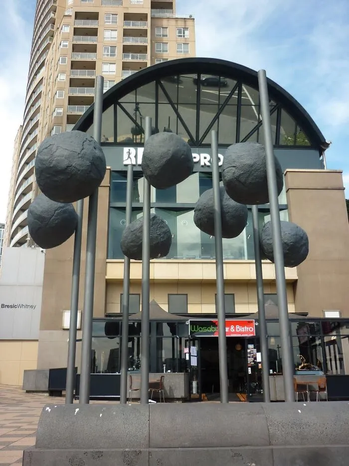 Public art installation featuring large grey boulder-like structures mounted high on metal poles.