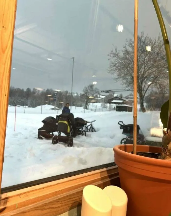 Snowy landscape reflected in window with strollers outside on a winter day