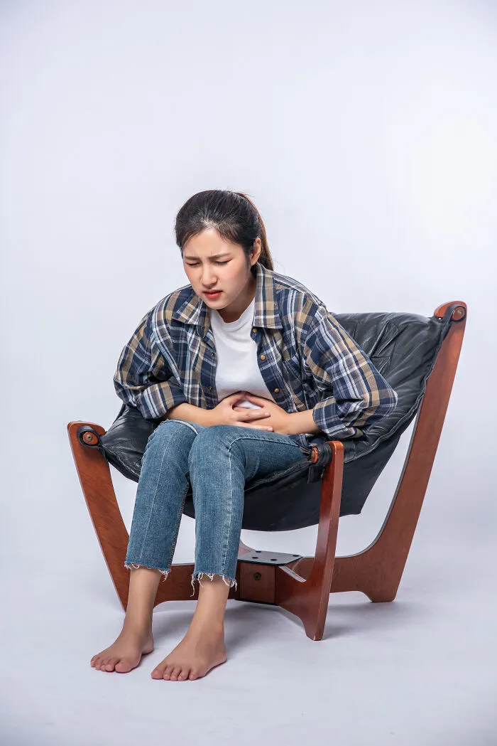 A young woman sitting in a chair holding her stomach, showing signs of Gen Z health problems.
