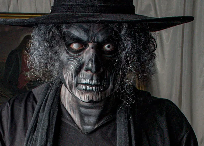 Haunted house worker wearing scary skeleton face paint with black hat