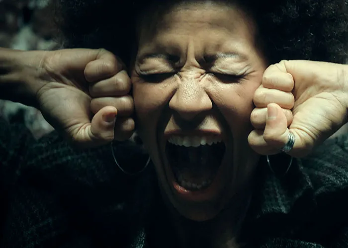 Terrified woman screaming with fists near face in haunted house