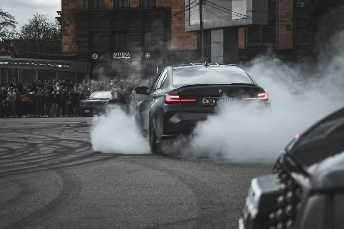 Black car performing a burnout with smoke in a street crowd scene for BF phone shock