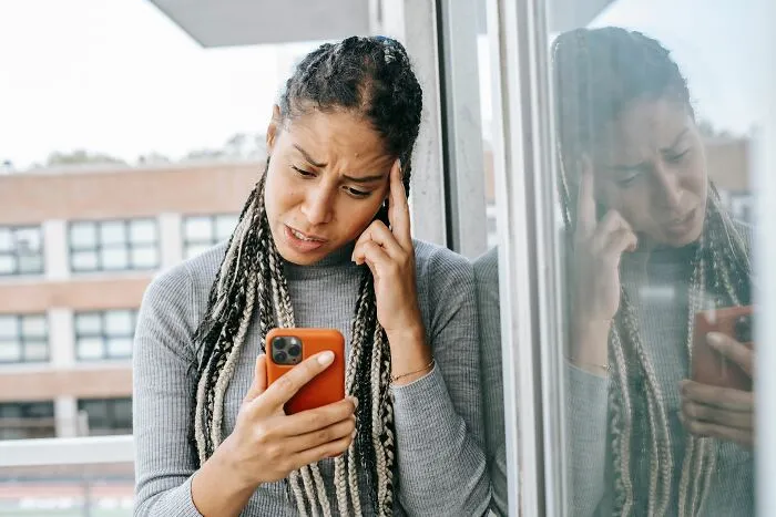 Worried woman looking confused at her phone near window