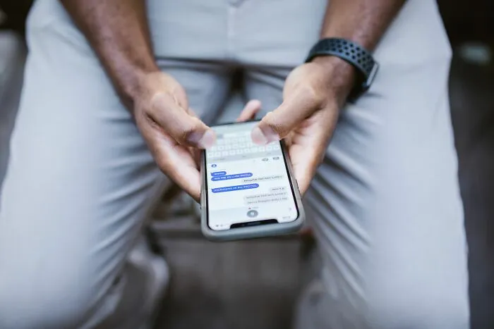 Person texting on their phone holding it with both hands sitting down