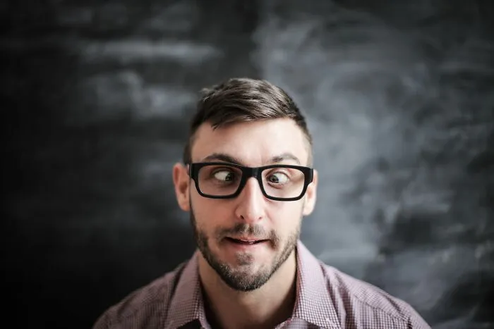 Man with glasses making a funny face in front of blackboard