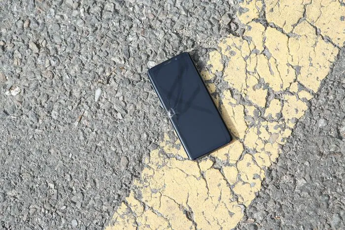 Broken phone with cracked screen lying on cracked asphalt near yellow line
