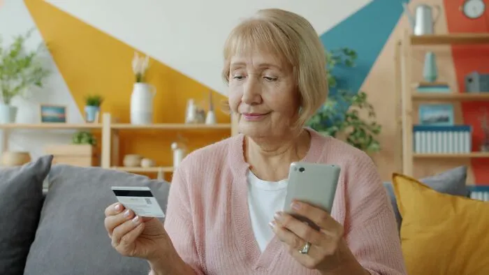 Older woman holding credit card and smartphone indoors