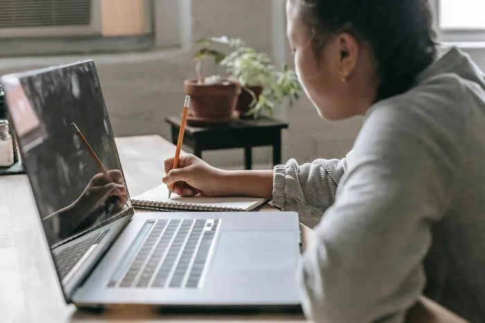 Student writing notes while using a laptop for online learning