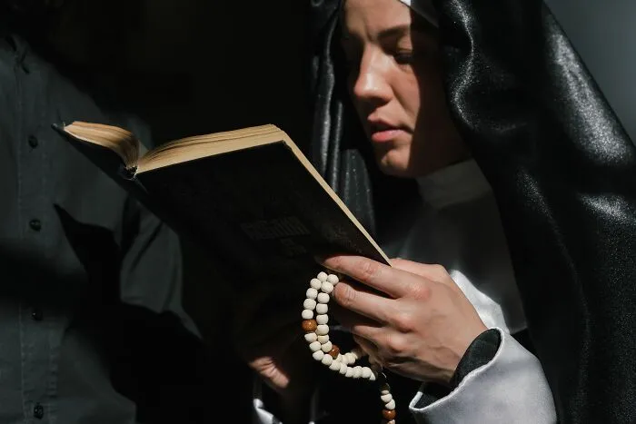 Nun holding a book and rosary beads in a focused religious moment