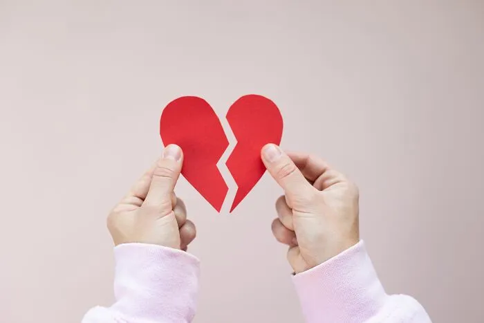 Hands holding two halves of a torn red paper heart, symbolizing people behaving like the world owed them everything