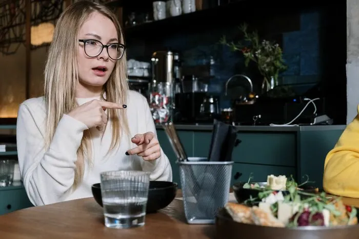 A blonde woman in glasses pointing and speaking to show people behaving like the world owed them everything.