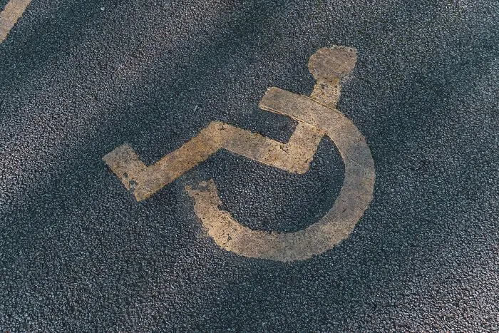 An old disabled parking symbol painted on asphalt, showing people behaving like they are owed everything