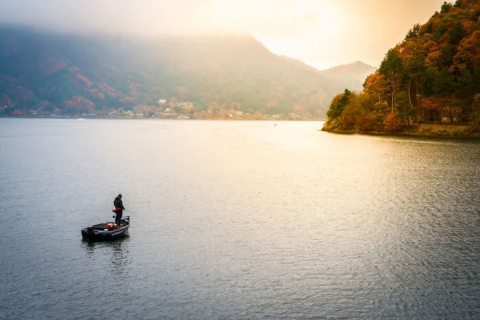 A lonely person fishing on a calm lake, surrounded by mountains after life fell apart.