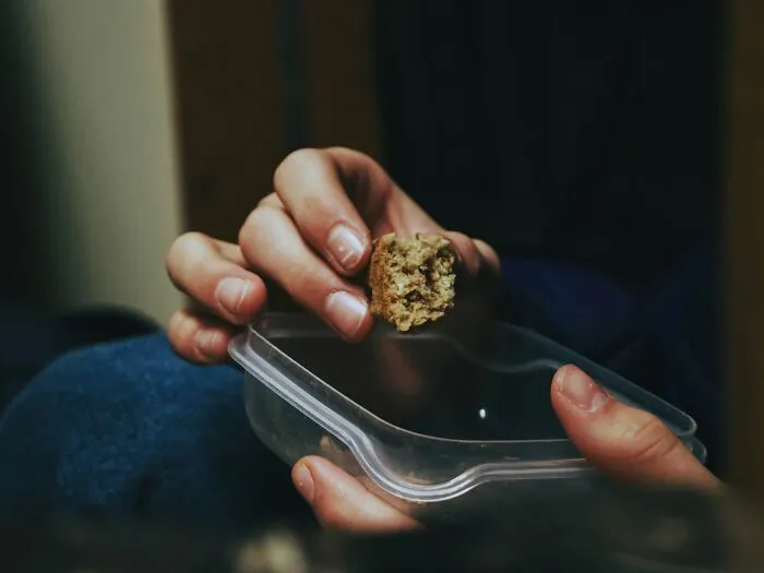 Close up of hands holding a piece of food over a plastic container in a sobering story about life mistakes