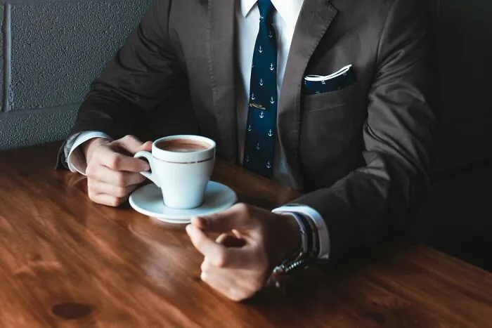A man in a suit drinking coffee at a wooden table, representing life moves.