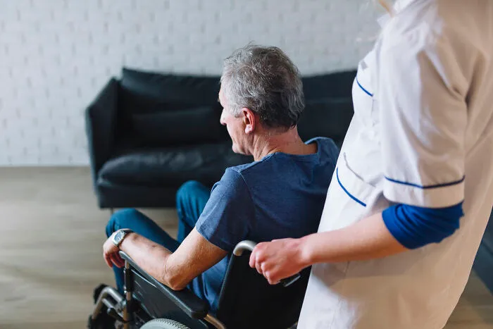 A nurse pushing a senior man in a wheelchair, representing sobering stories of sudden change.